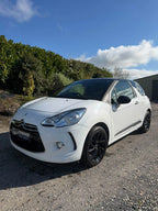 A white Citroèn DS3 Grand Picasso parked outdoors on a gravel surface, with trees and a blue sky in the background.