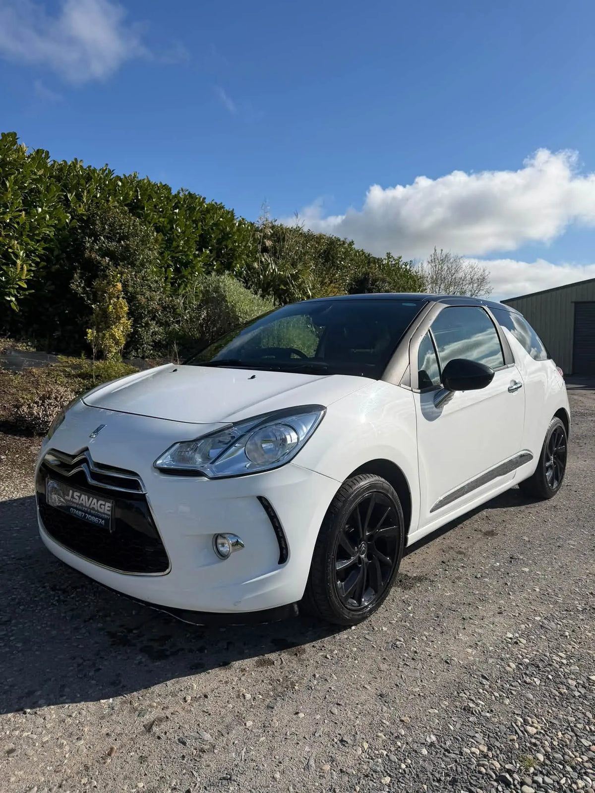 A white Citroèn DS3 Grand Picasso parked outdoors on a gravel surface, with trees and a blue sky in the background.