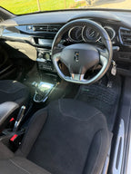 A clean, front-facing view of a car's interior, showing the black fabric seats, steering wheel, dashboard, and gear shift console. The DøSER logo is visible on the steering wheel center.