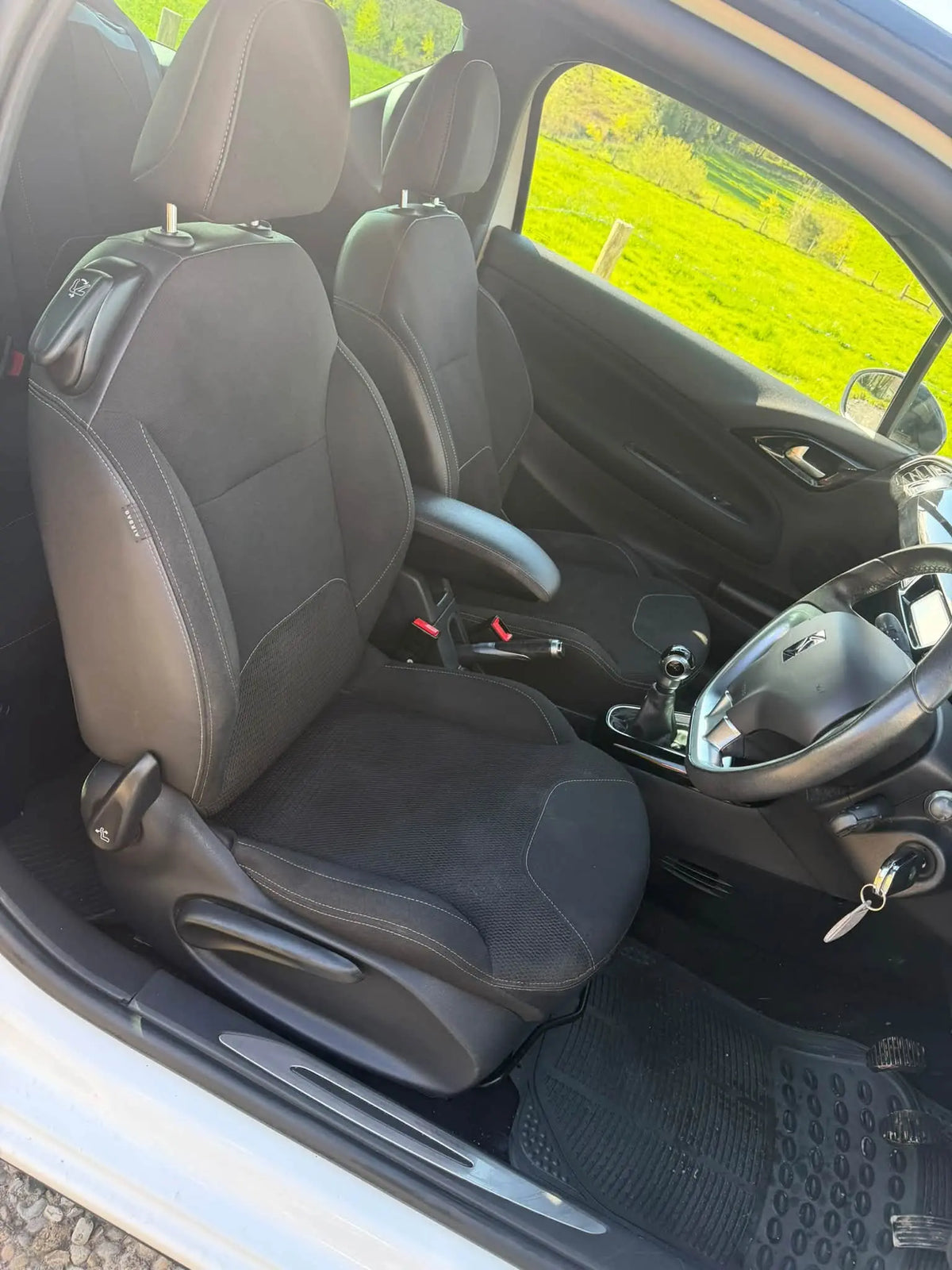 Black fabric car seats in a vehicle interior, with the front passenger seat and center console visible, photographed from the open driver's side door.